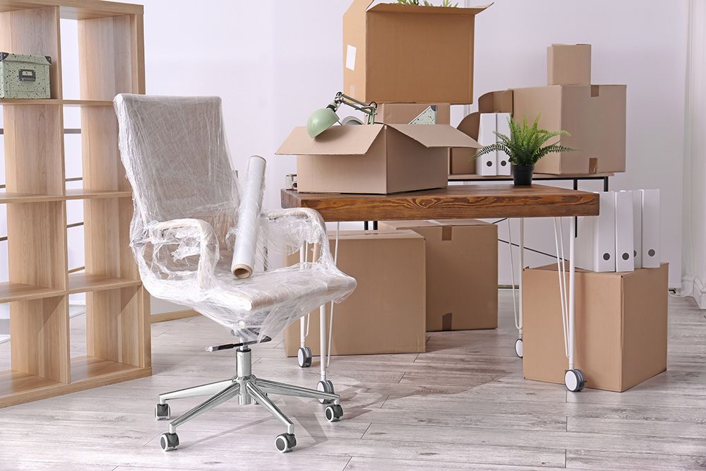 Ein Bürostuhl eingepackt in Folie und drumherum stehen Umzugskisten